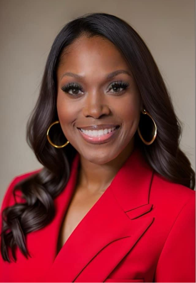 Portrait photo of Kimberly Hill. She has dark skin and dark hair. She is wearing a red suit and is smiling in the photo